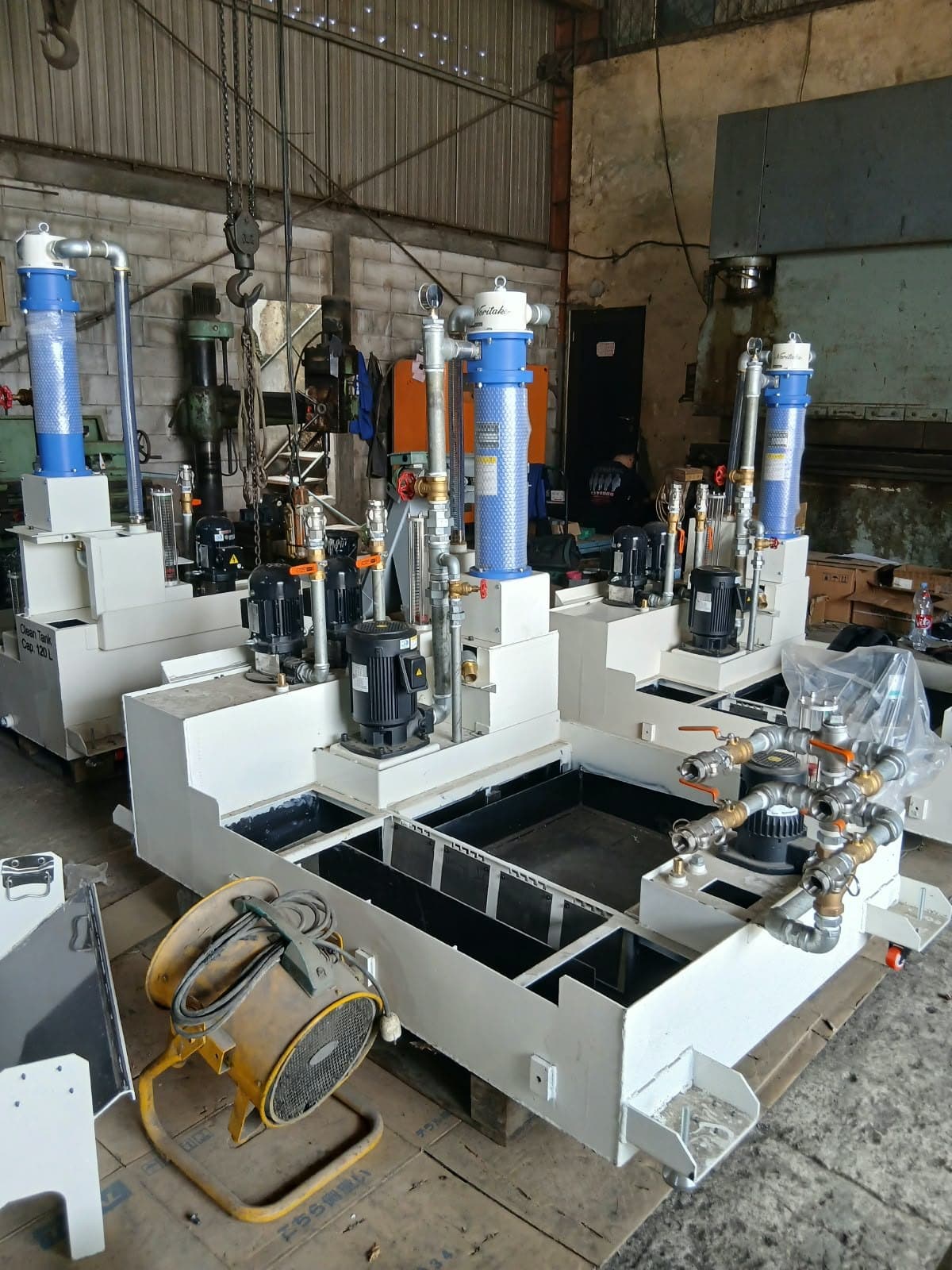Mesin pencuci komponen industri berwarna putih dengan housing filter biru, di lantai bengkel
