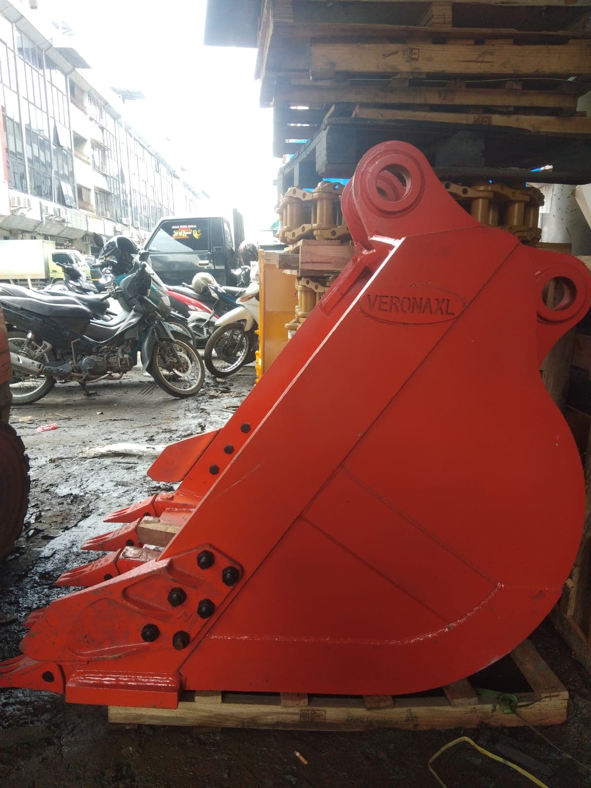 Bucket excavator merah dengan cutting edge sistem baut, di atas palet